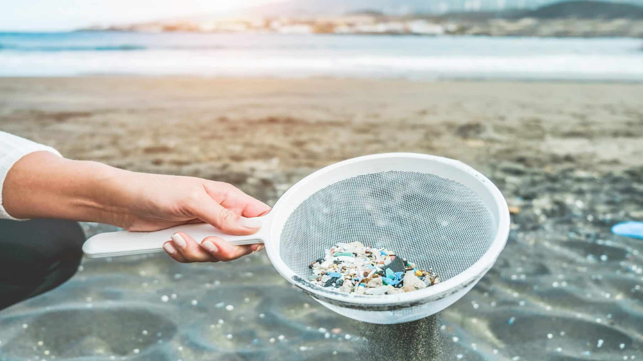 A woman cleans microplastics from sand on the beach.