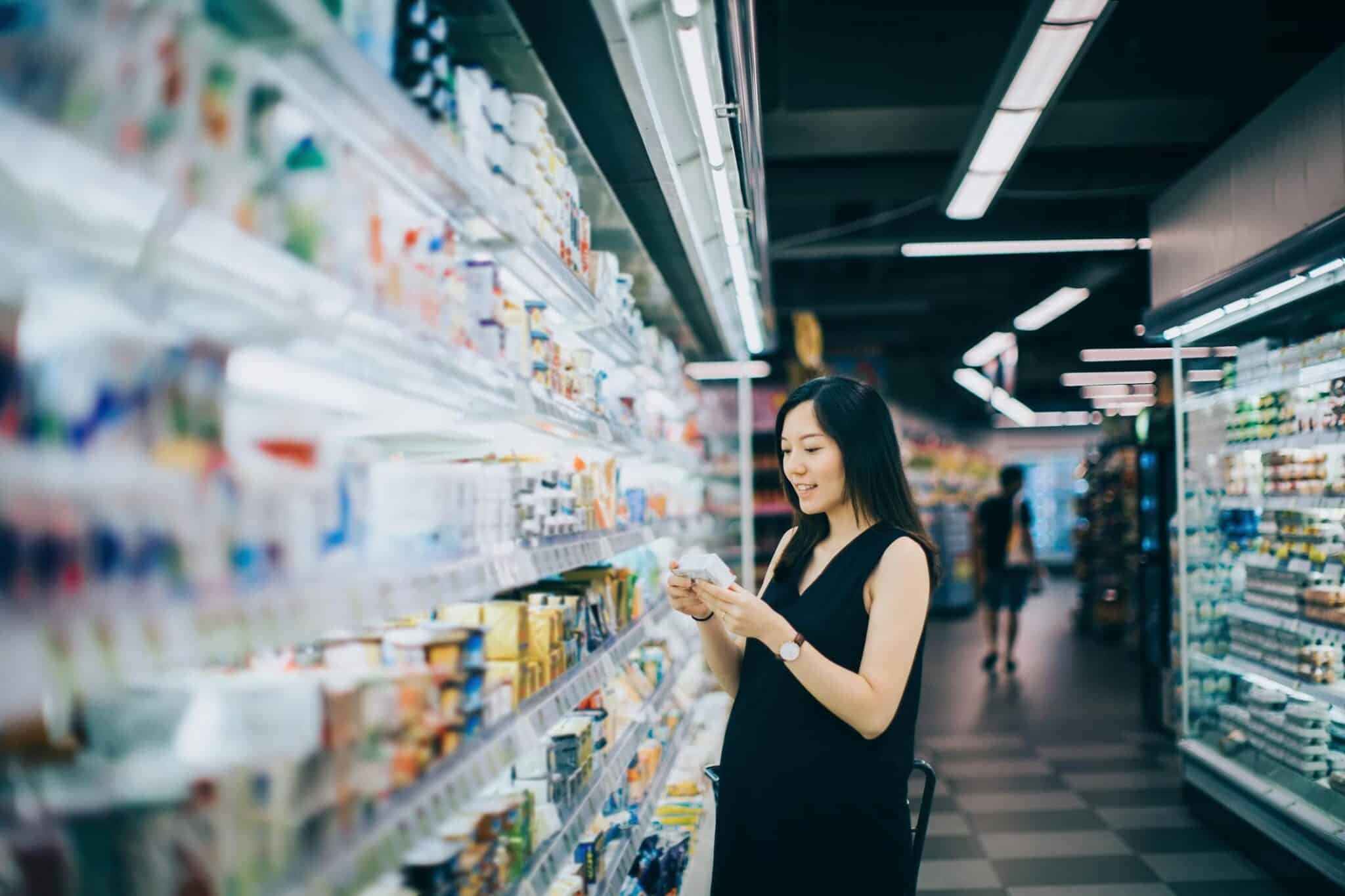 woman grocery shopping in supermarket and reading nutrition label on a packet of cheese 