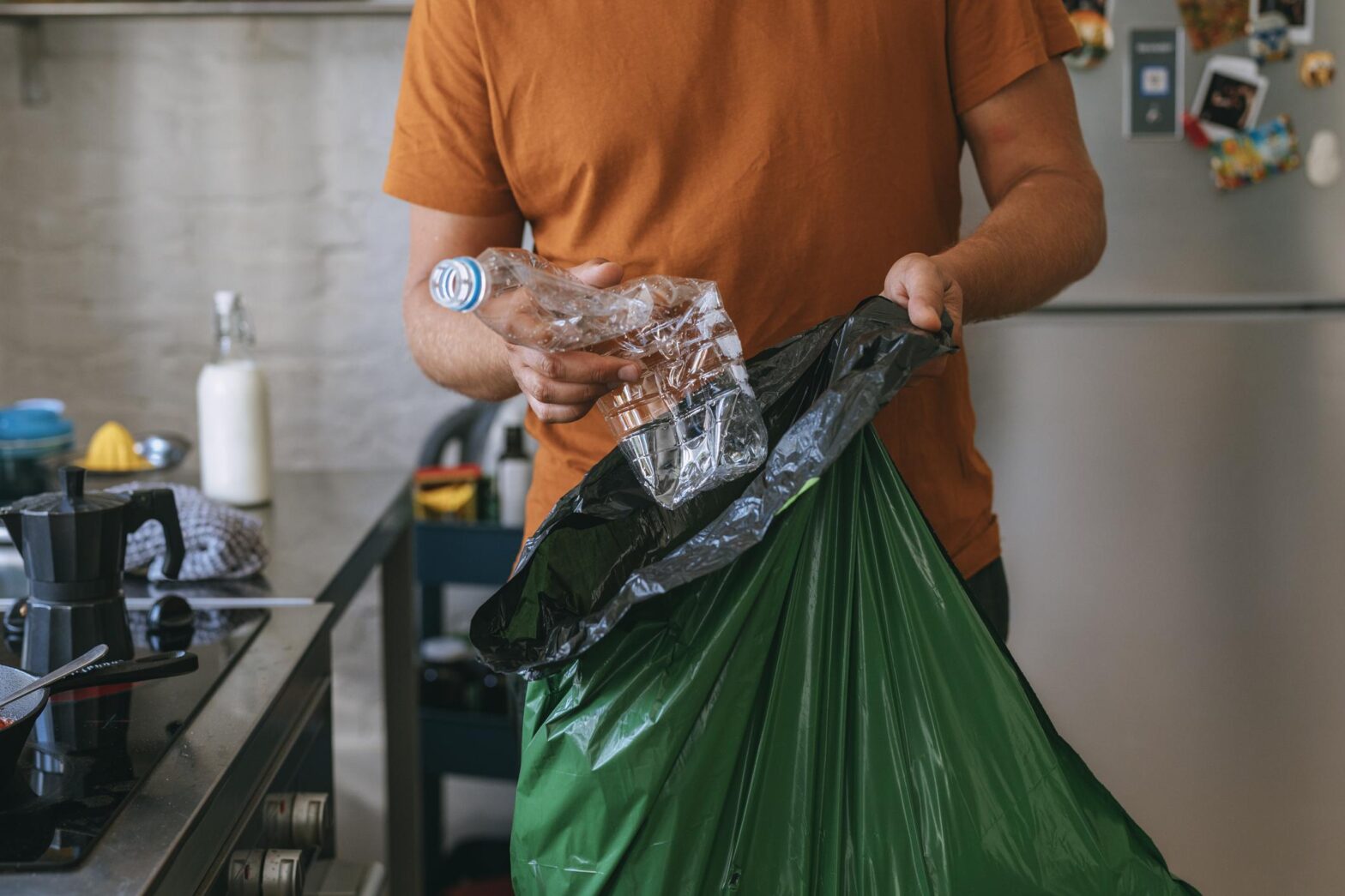 man puts plastic water bottle into green trash recycling bag