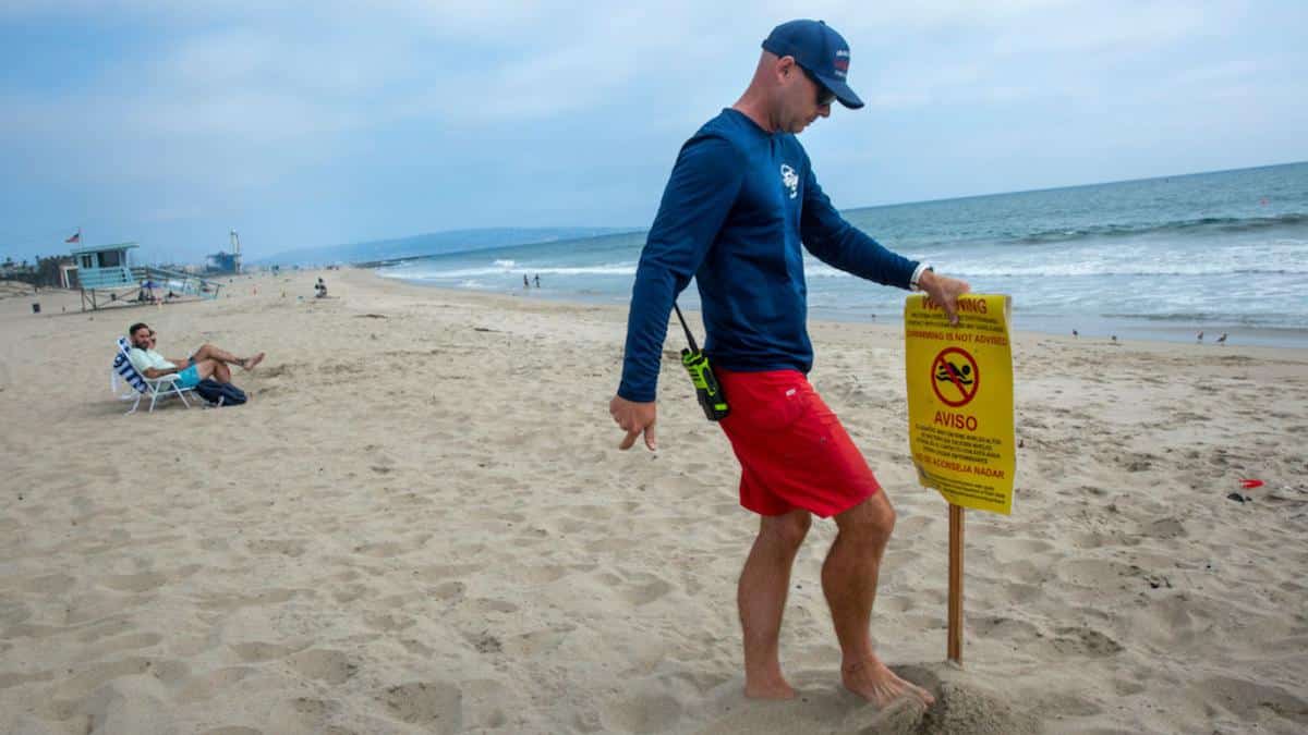 A lifeguard puts out a sign warning that swimming is not advised.