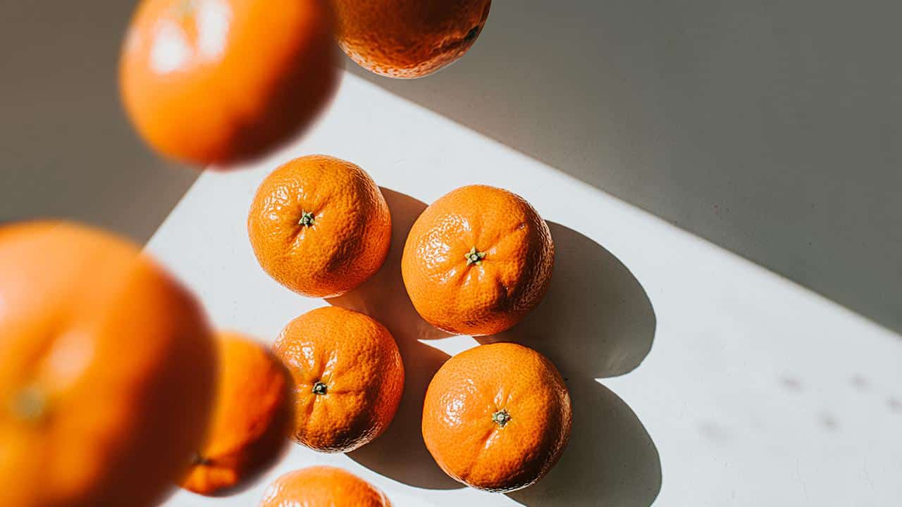 Mandarin oranges sit on a white surface while others fall from above