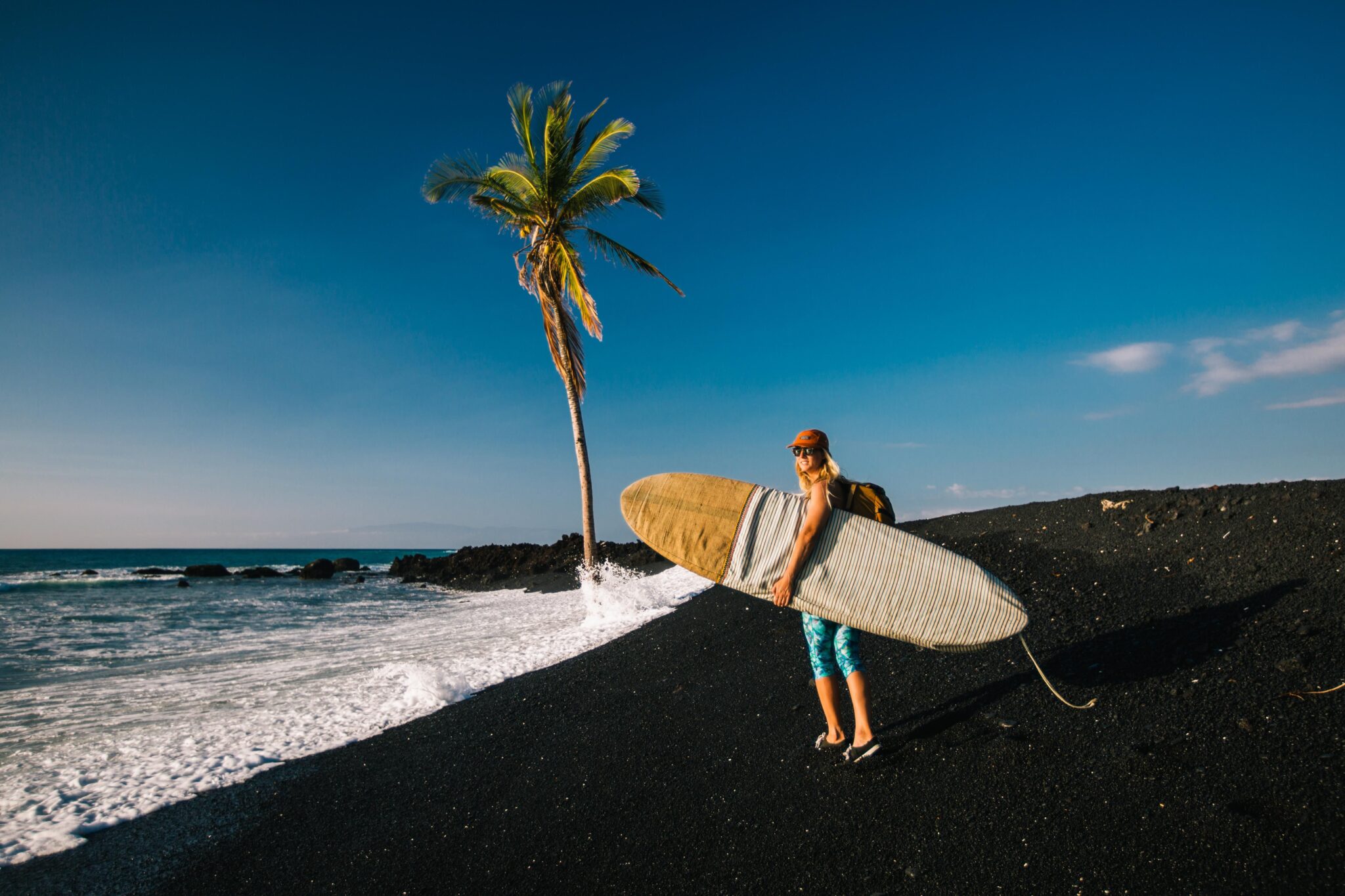 A woman carries a surfboard along a beach.