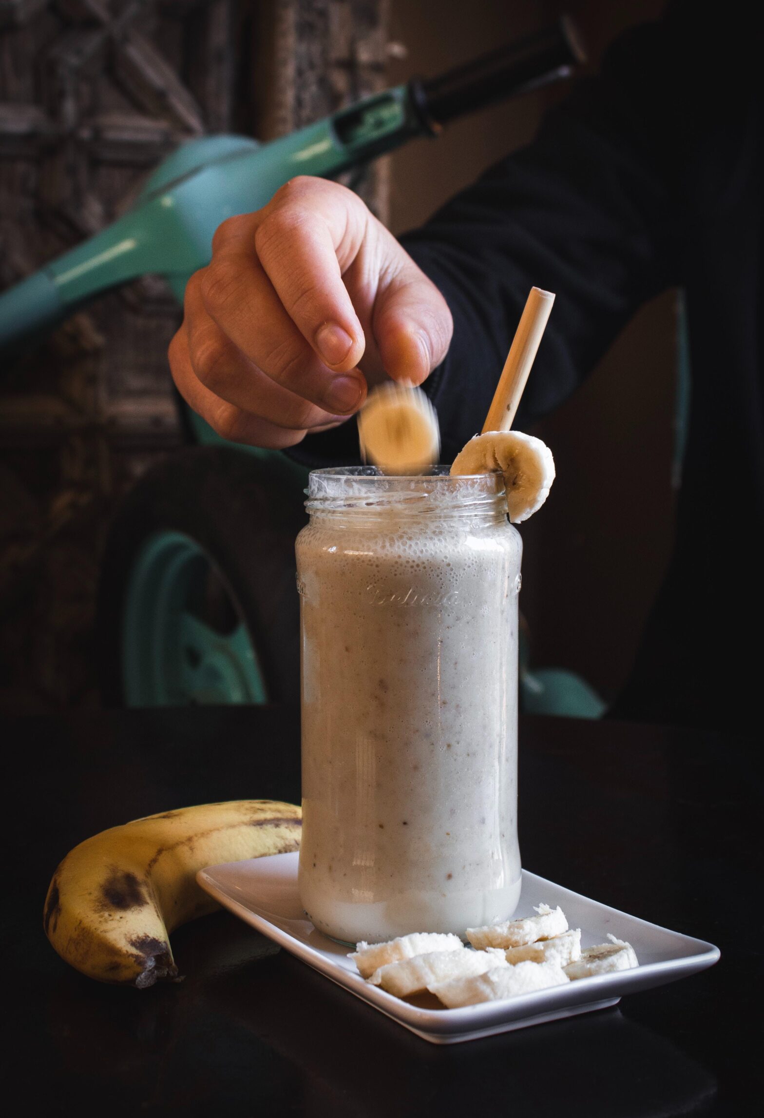 person putting sliced banana fruit in meal replacement powder shake
