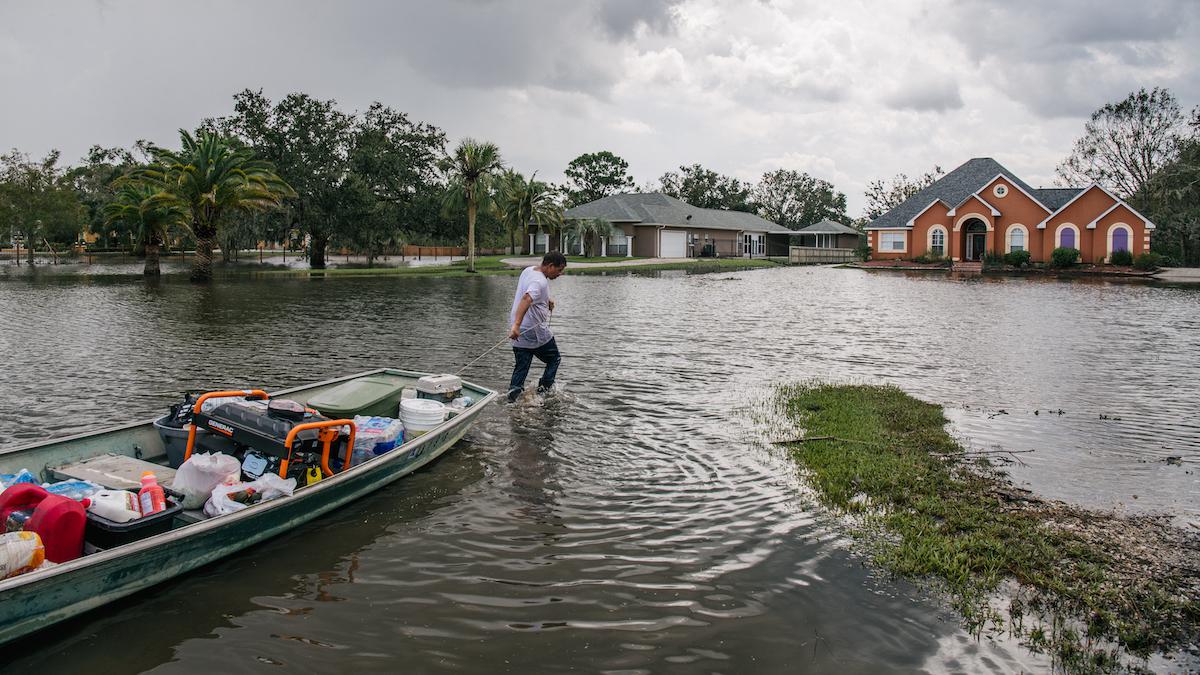 A man pulls a boat through a flooded neighborhood.
