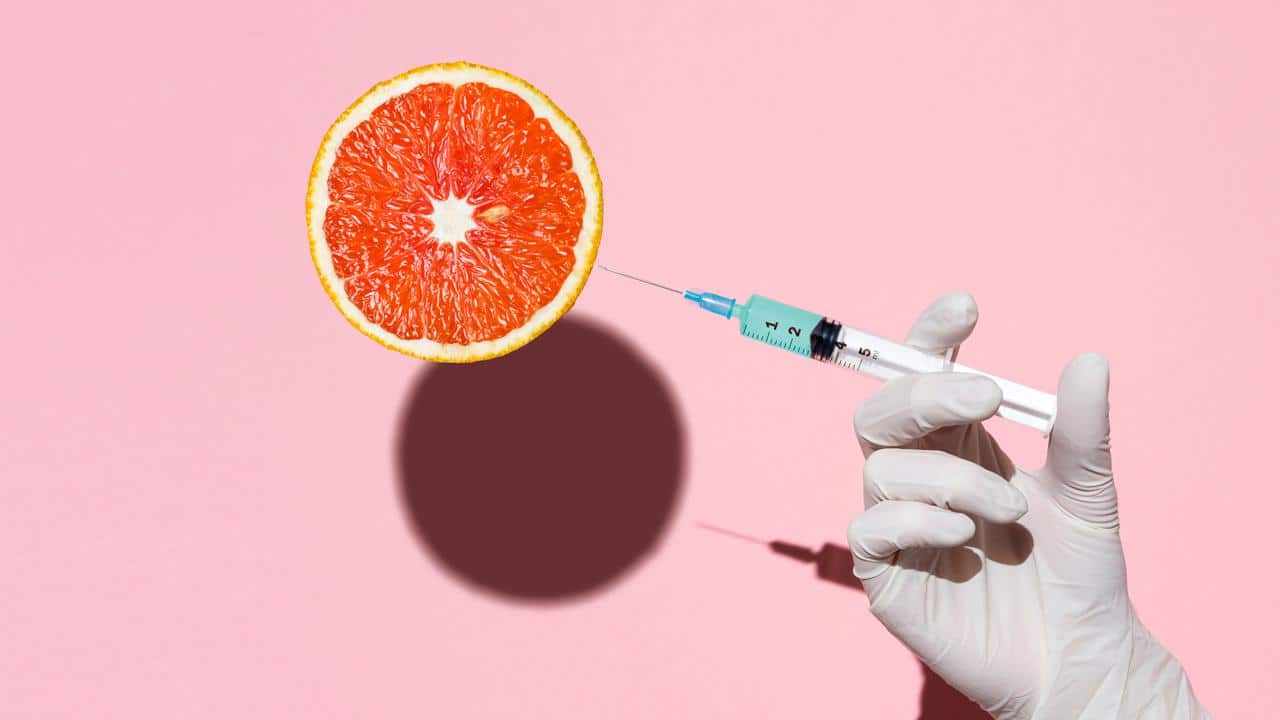 Doctor's hand holding syringe injecting fluid into an orange fruit