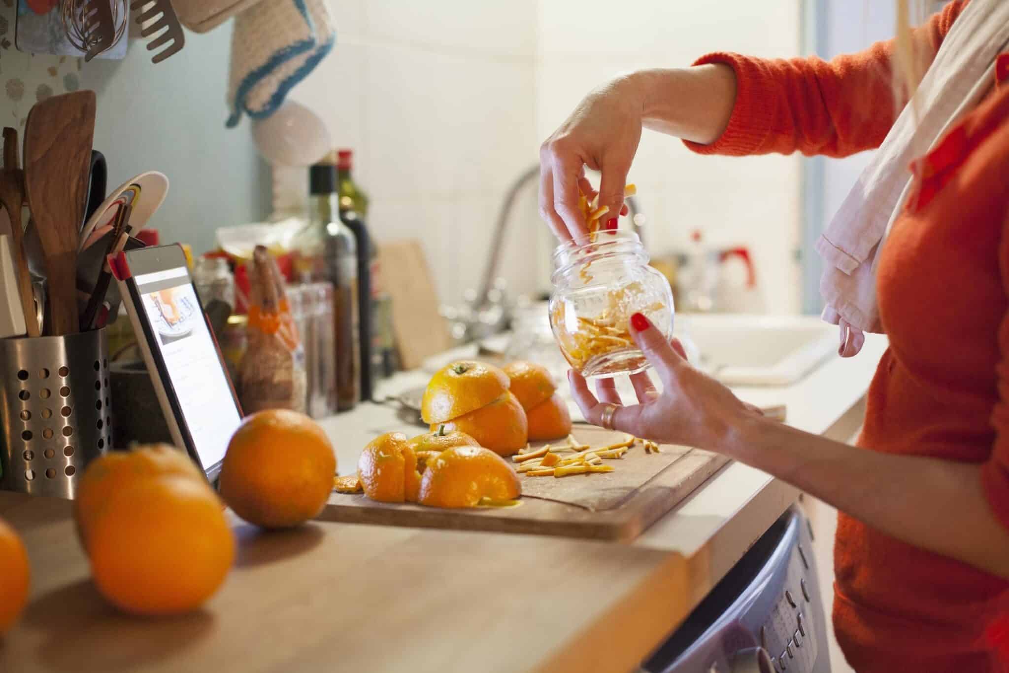 Woman preparing to make orange marmalade, filling jar with thinly cut orange zest