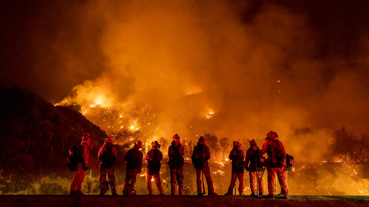 A group of inmate firefighter watch as wildfire burns