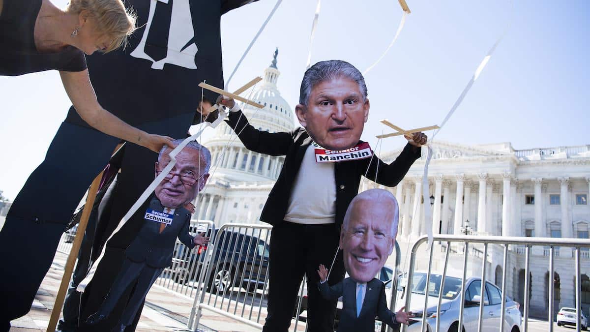 Activists from Greenpeace USA set up a marionette depicting Joe Manchin, President Joe Biden and Chuck Schumer.