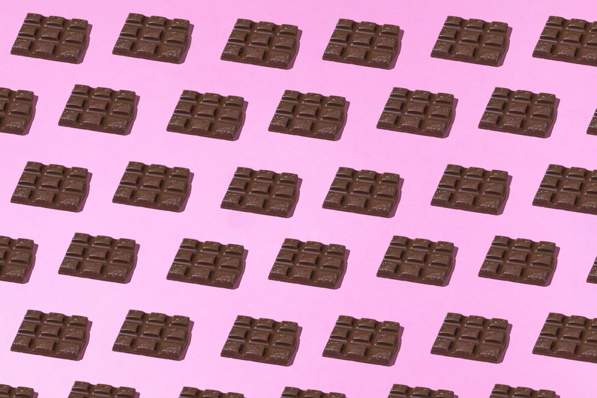 Chocolate tablets pattern with hard shadow on pink background