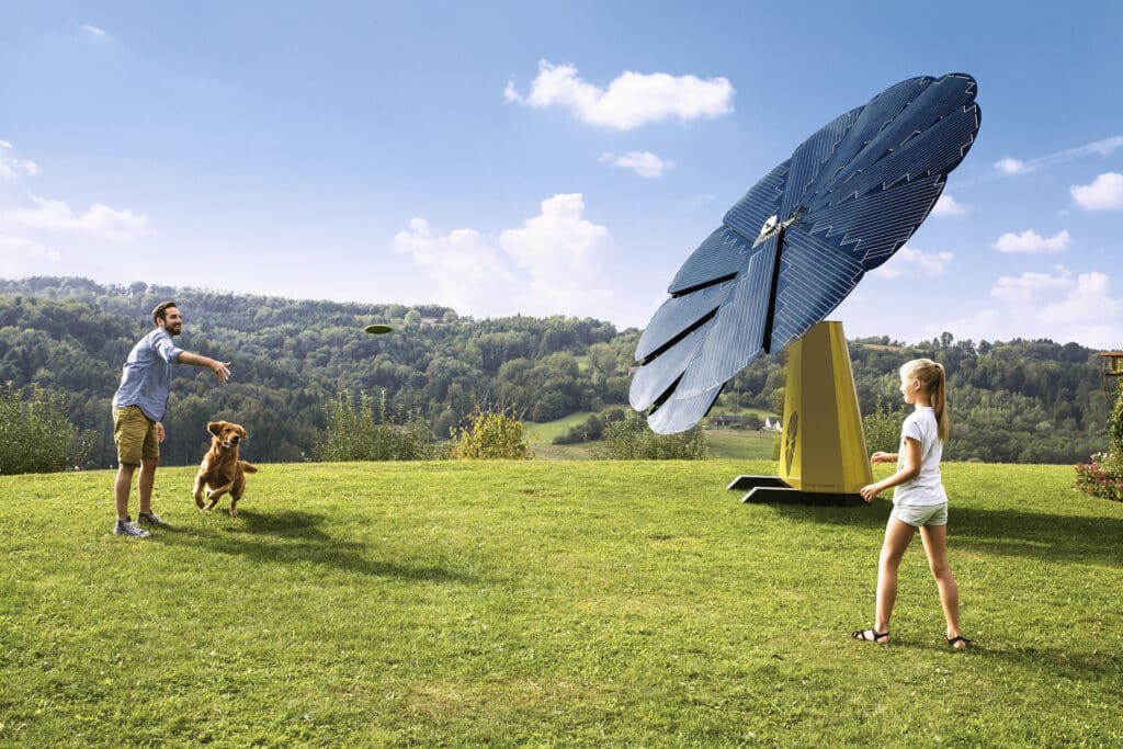 Smartflower solar flower on lawn with two people and dog playing Frisbee