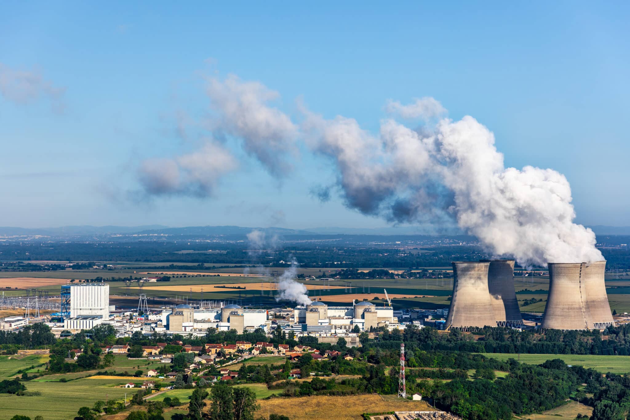 French nuclear power station aerial view in countryside landscape in summer with smoking cooling towers on blue sky