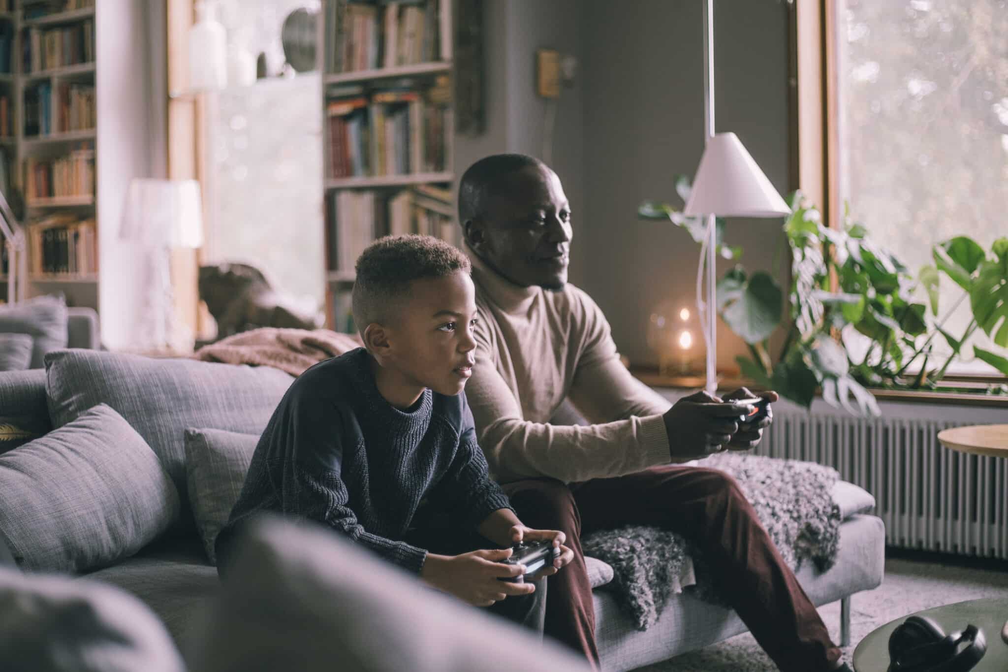 Smiling father and son playing video game while sitting on sofa at home