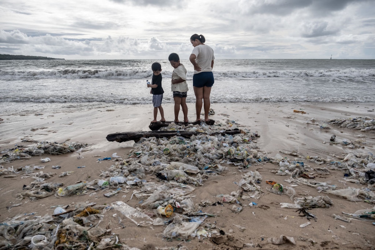 People stand among plastic trash on a beach in Indonesia.