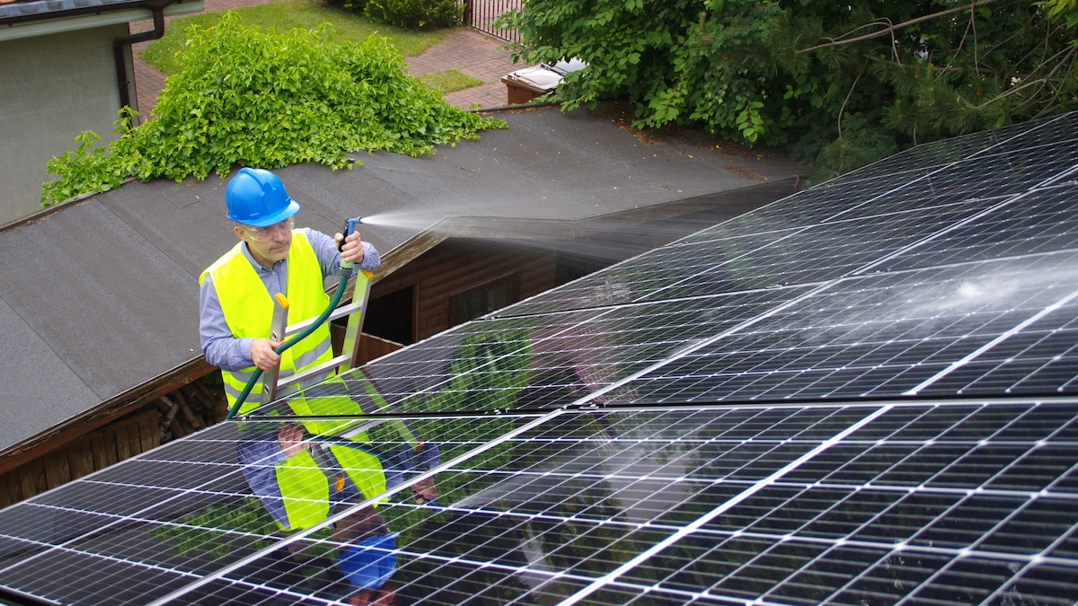 A man cleans a solar panel with water.