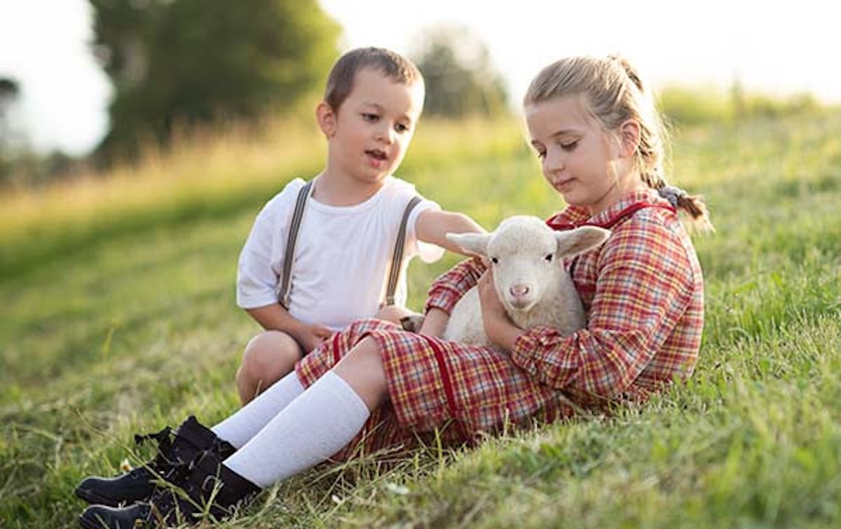 Two children hold and pet a lamb.