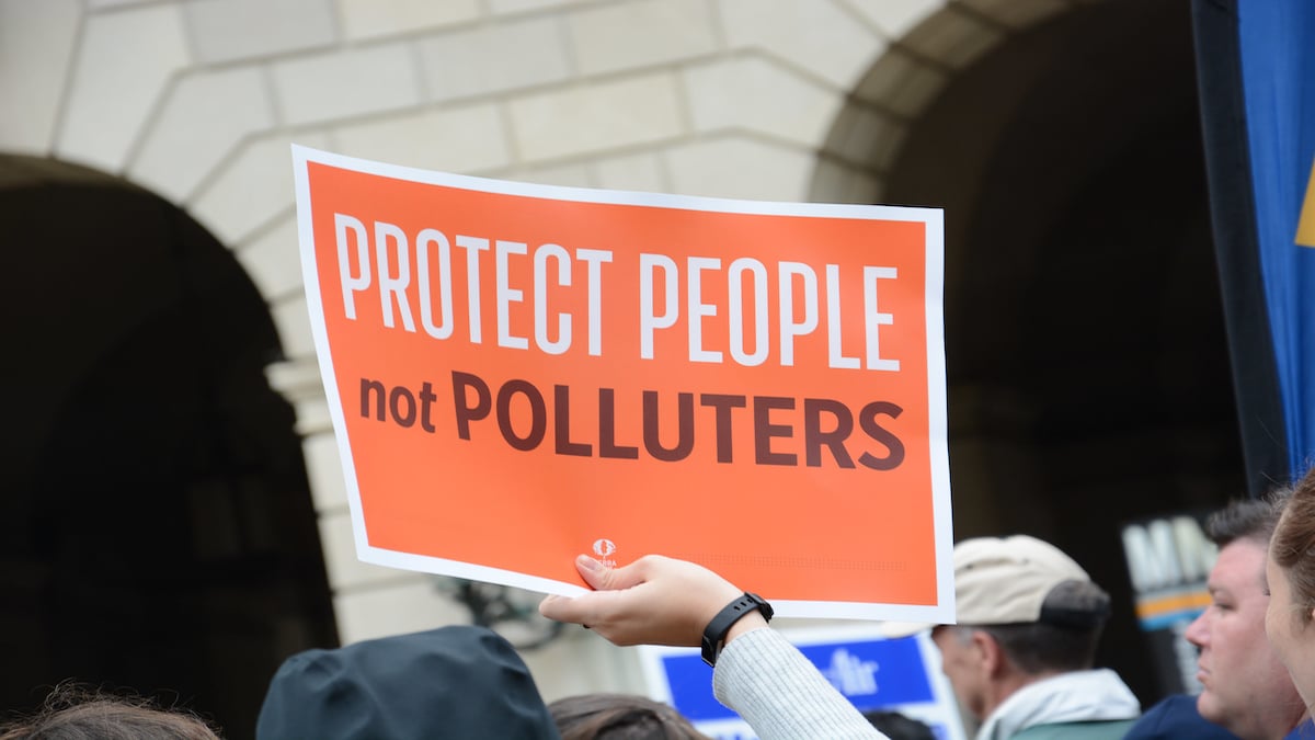 A protester outside of EPA headquarters holds a sign saying "Protect People Not Polluters."
