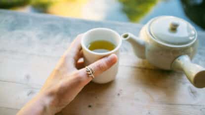 Hand Holding Green Tea Cup By Teapot On Table
