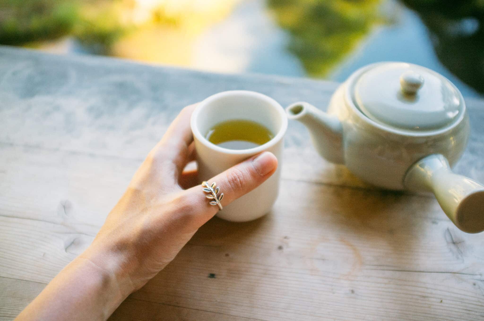 Hand Holding Green Tea Cup By Teapot On Table