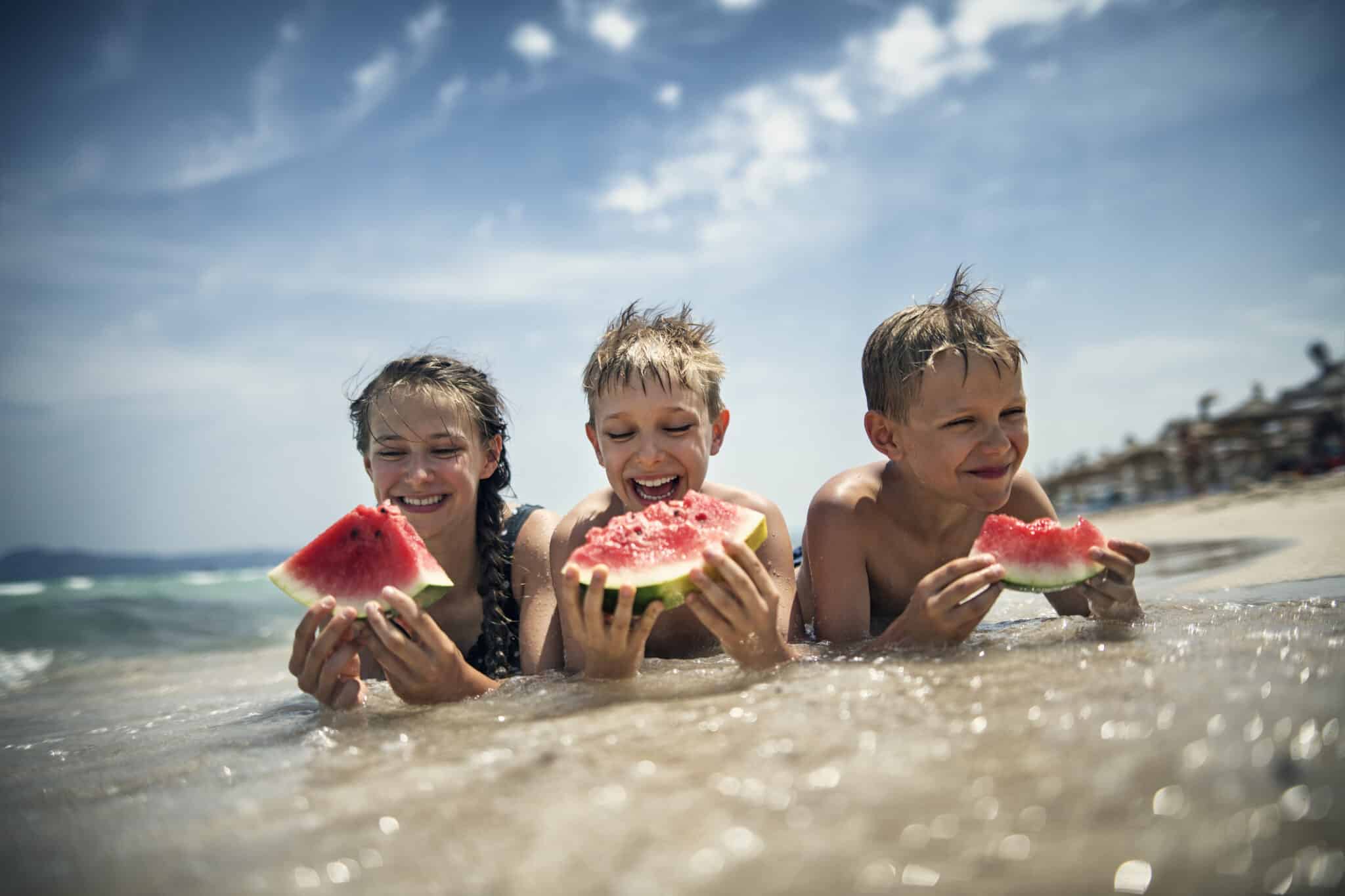 Happy kids eating watermelon on the beach
