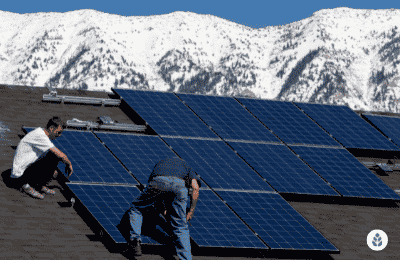 two men installing solar panels on a house roof overlooking snowy mountains