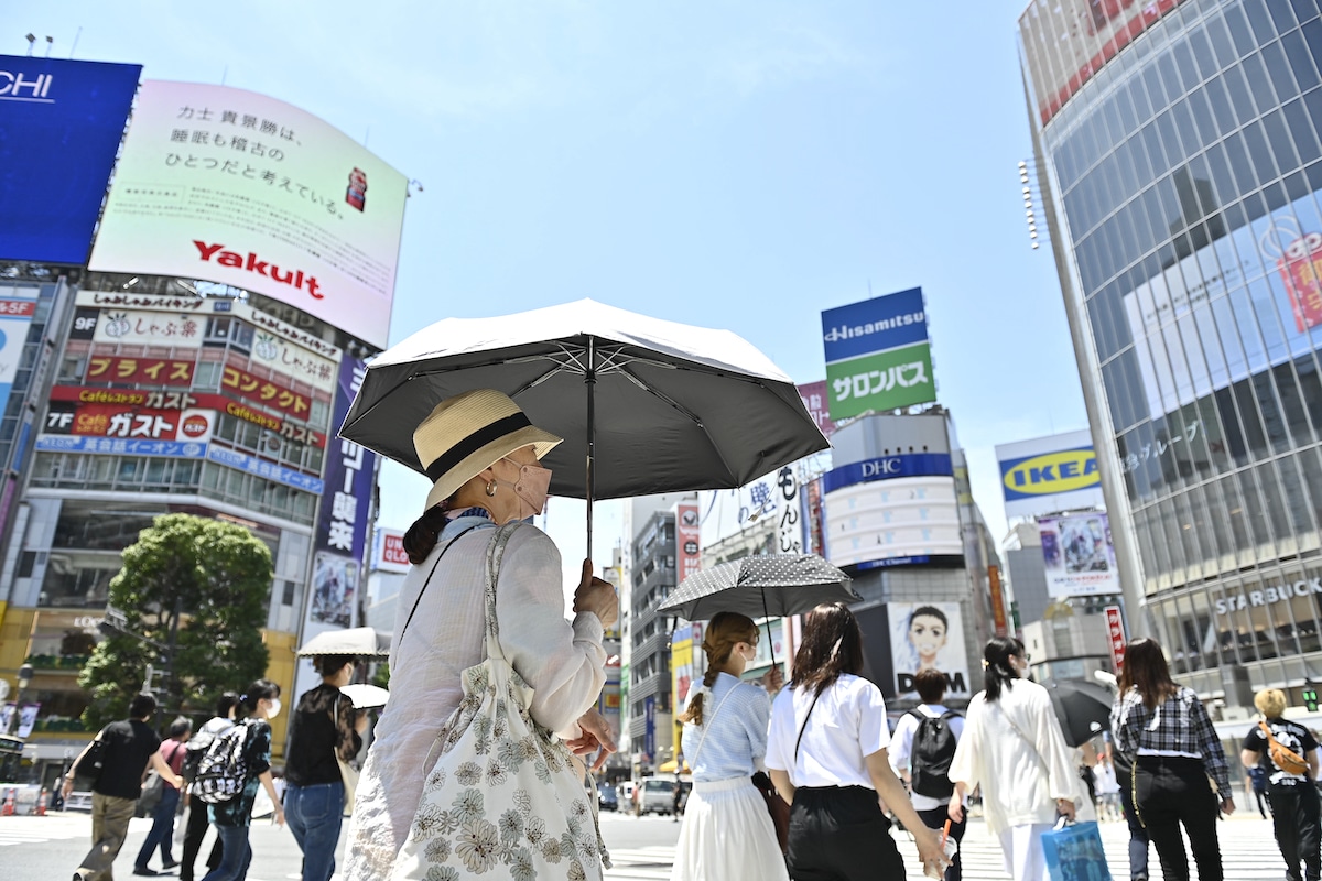 People walking in Tokyo's Shibuya district with umbrellas to protect themselves from the sun
