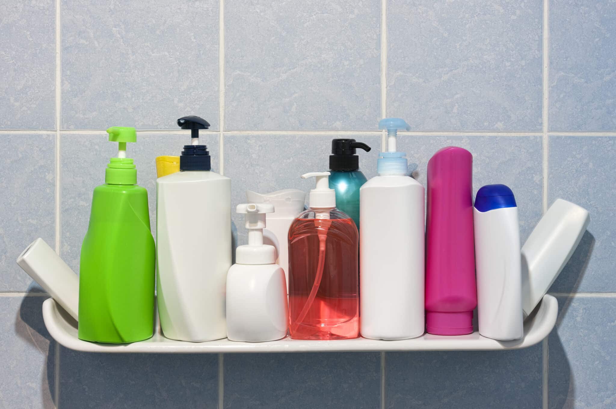 Many shampoo and soap bottles on a bathroom or shower shelf.