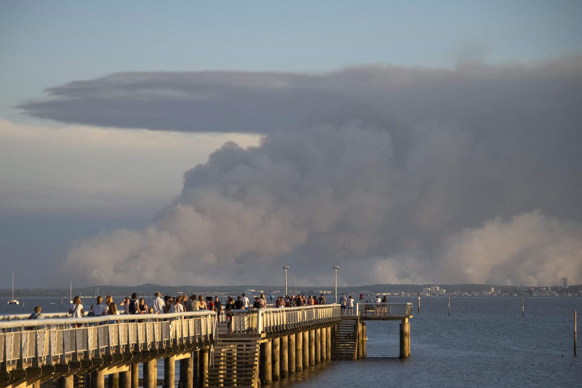 Tourists watch wildfire smoke on the shoreline in southwestern France