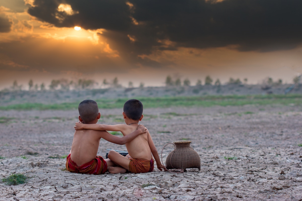 Two boys sit on ground parched from extreme climate change