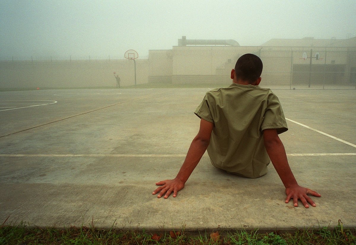 A boy sits in the fenced outdoor recreation area at Liberty County jail in Texas