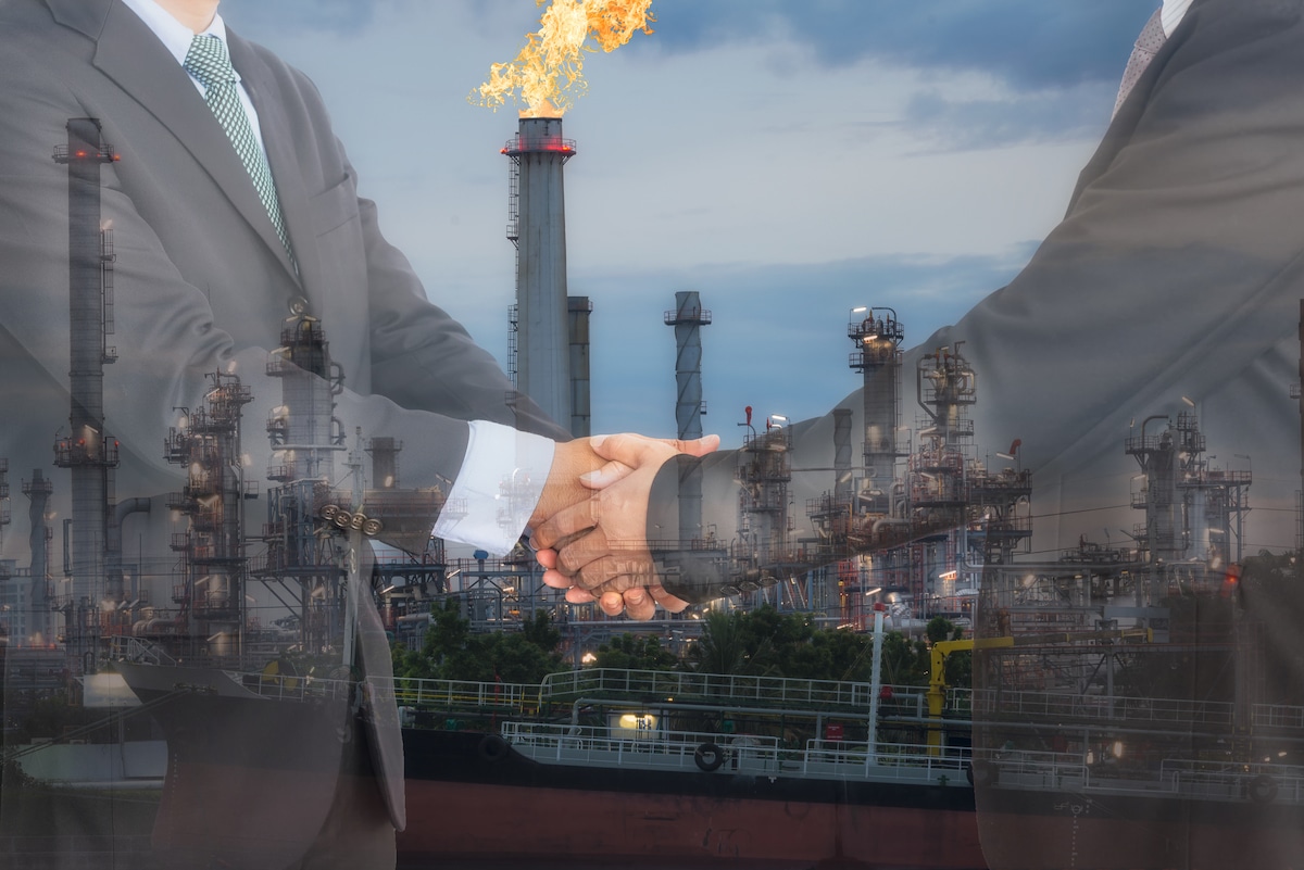 Businessmen shaking hands in front of an oil refinery