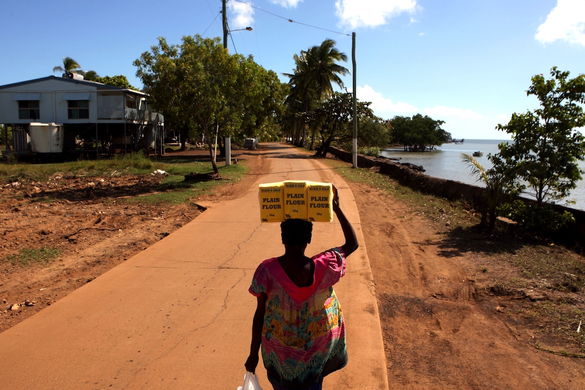 A woman walks home carrying flour on her head past a damaged sea wall on Saibai Island in the Torres Strait