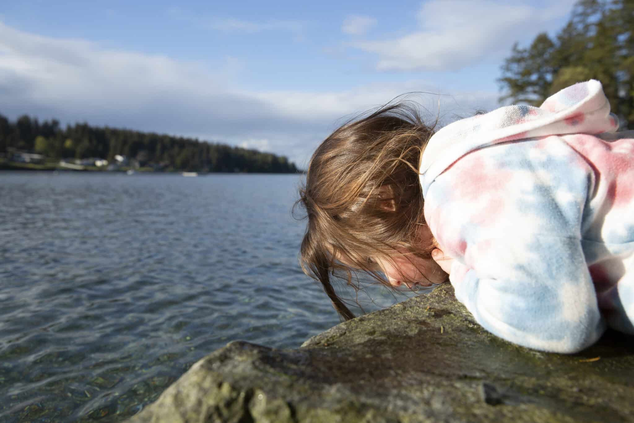 Toddler curiously looking over ledge into water searching for sea life