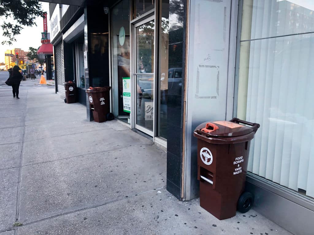 New Department of Sanitation food scraps and yard waste collection bins on sidewalks outside businesses, Queens, New York