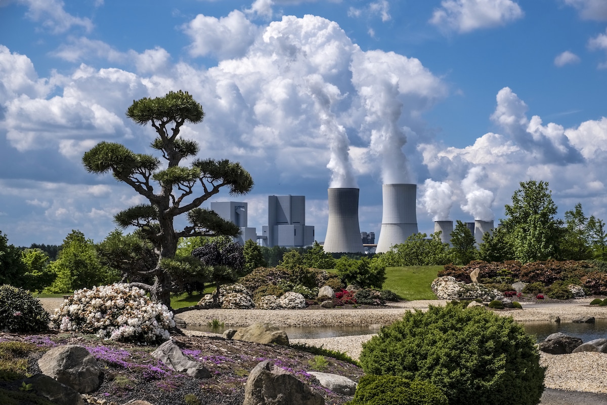 The buildings and steaming cooling towers of a coal-fired power plant behind a landscape park in Germany