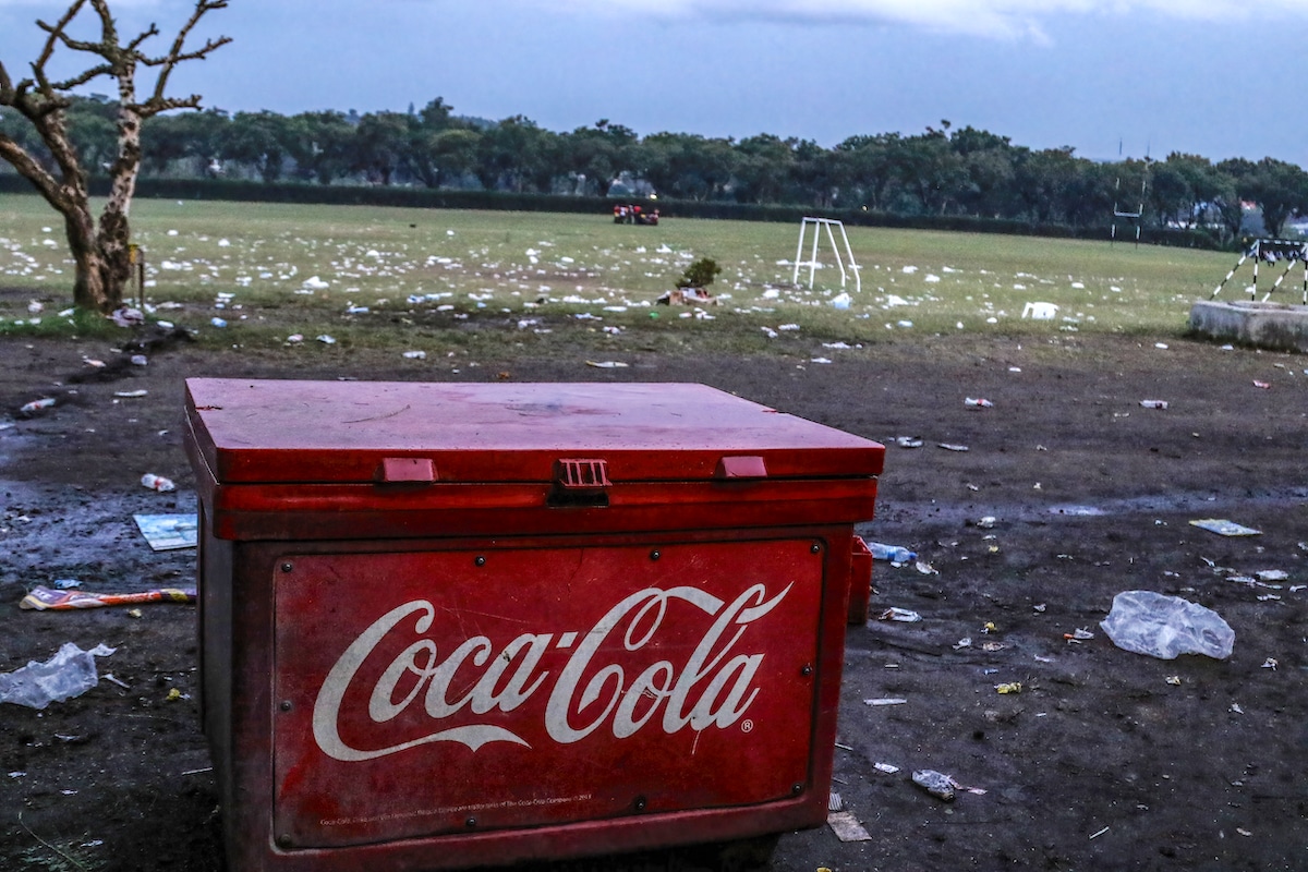 A Coca-Cola branded cooler box on a field littered with plastic bottles