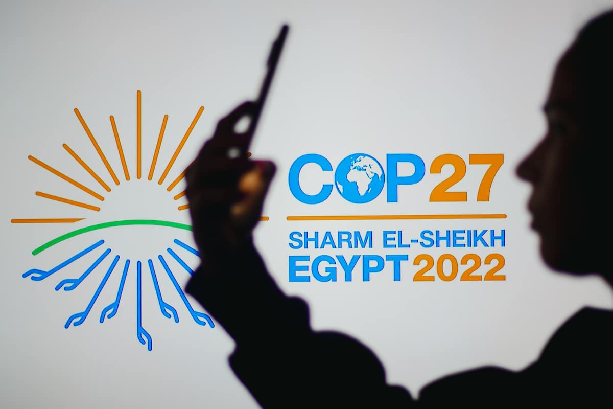 A woman holds a smartphone with the 2022 United Nations Climate Change Conference COP27 logo in the background