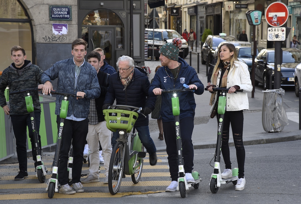 A group of people prepare to cross a busy city street on electric scooters in Paris, France