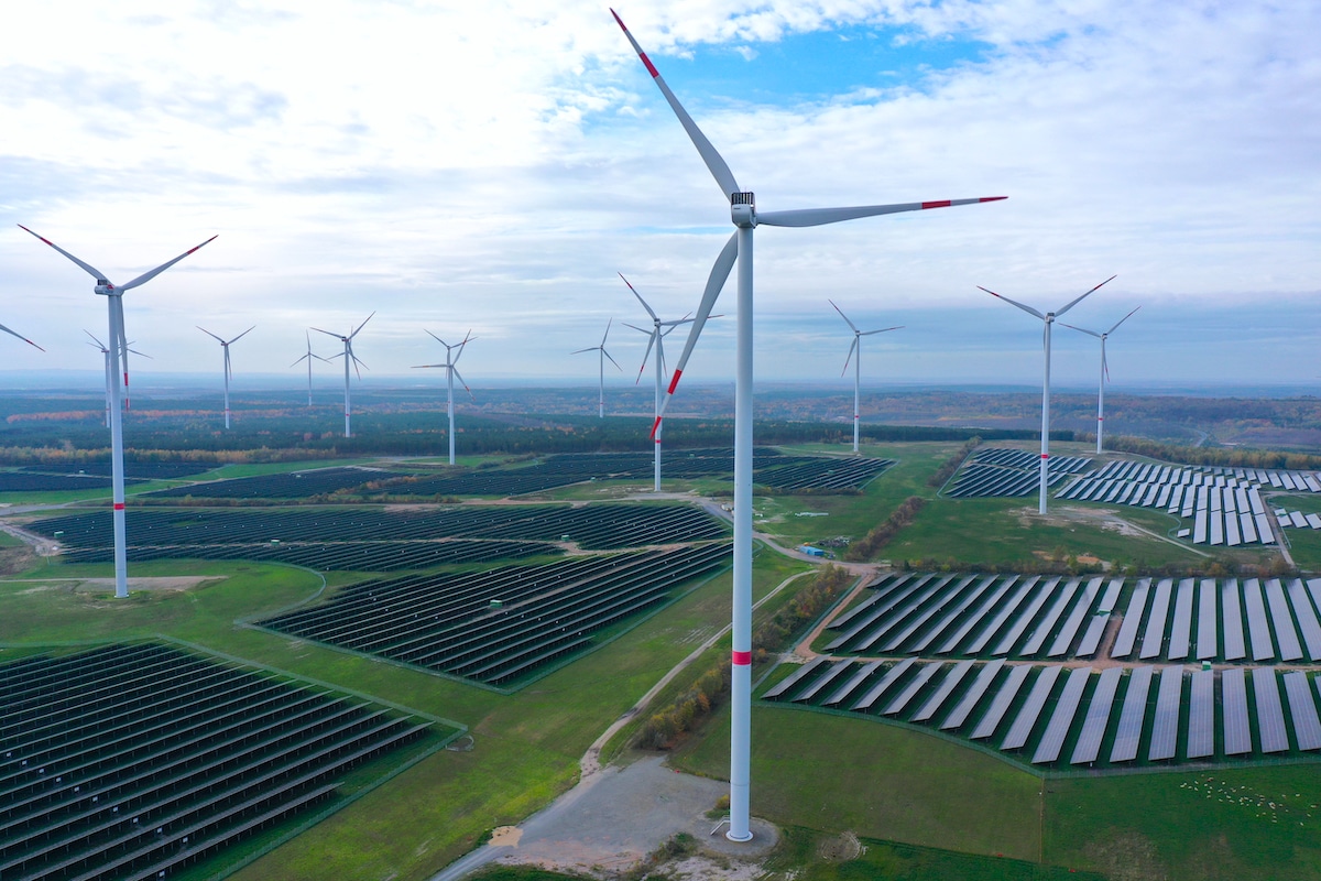 Wind turbines producing electricity spin over a solar park in Germany