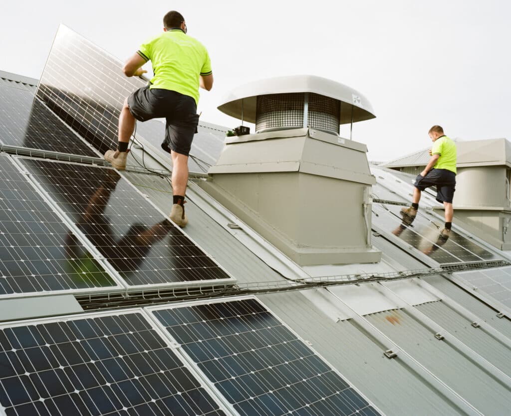Two people installing solar panels on a roof