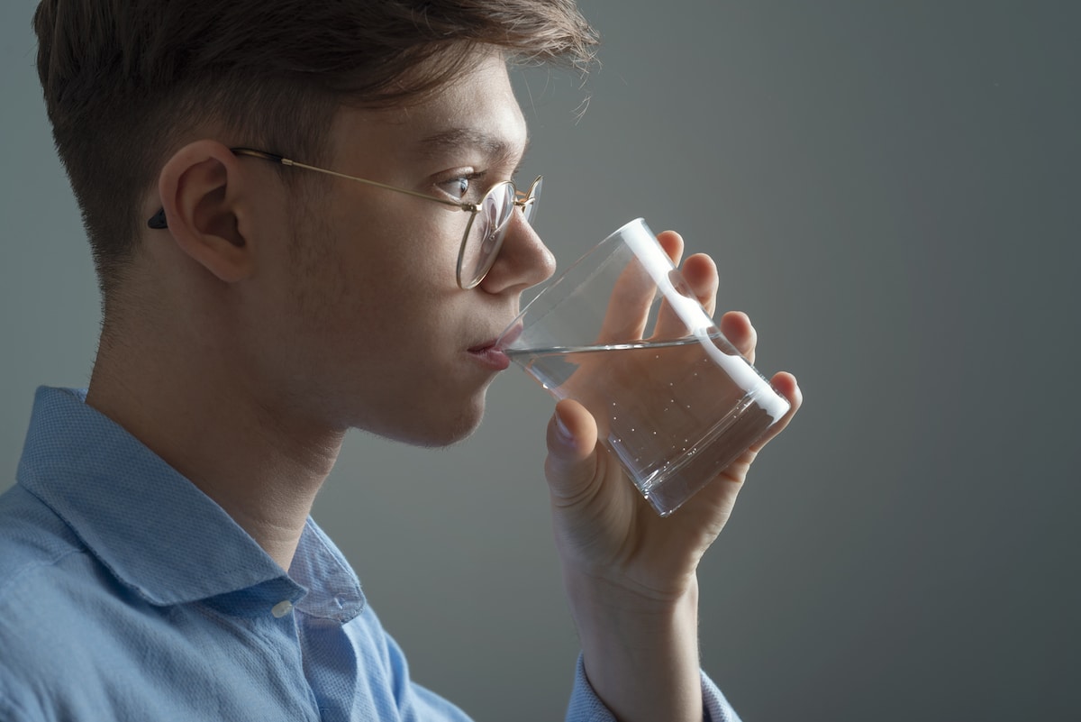 A young man drinking a glass of water. PFAS, which are commonly found in drinking water, can disrupt the metabolism and thyroid function of young adults