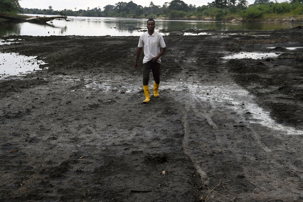 A farmer in NIgeria walks on a marshy shore of a river polluted by oil spills