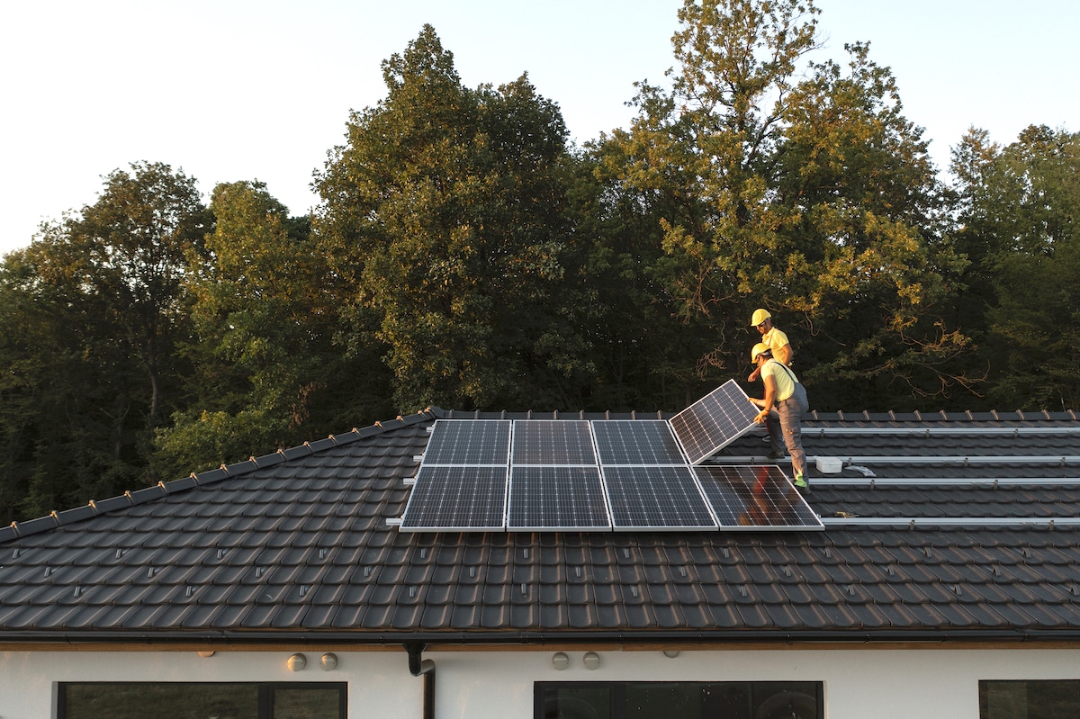 Two workers install solar panels on the roof of a house