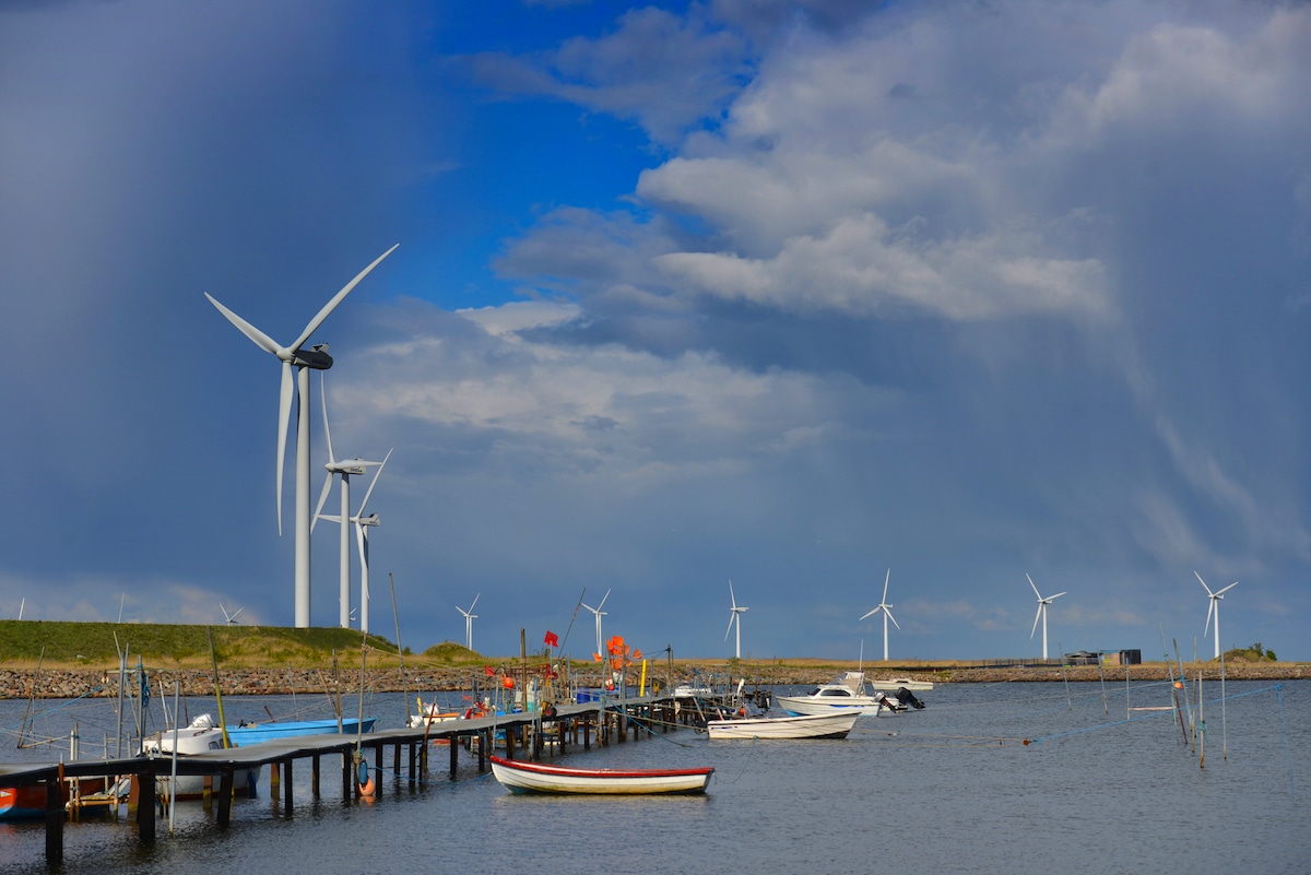 Nine Vestas wind turbines along the shore in Denmark on a sunny day with small boats in the water