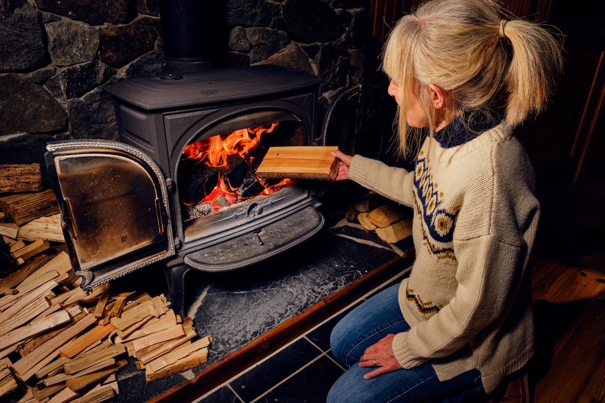 A woman in the UK puts a dried log into a glowing wood burning stove.