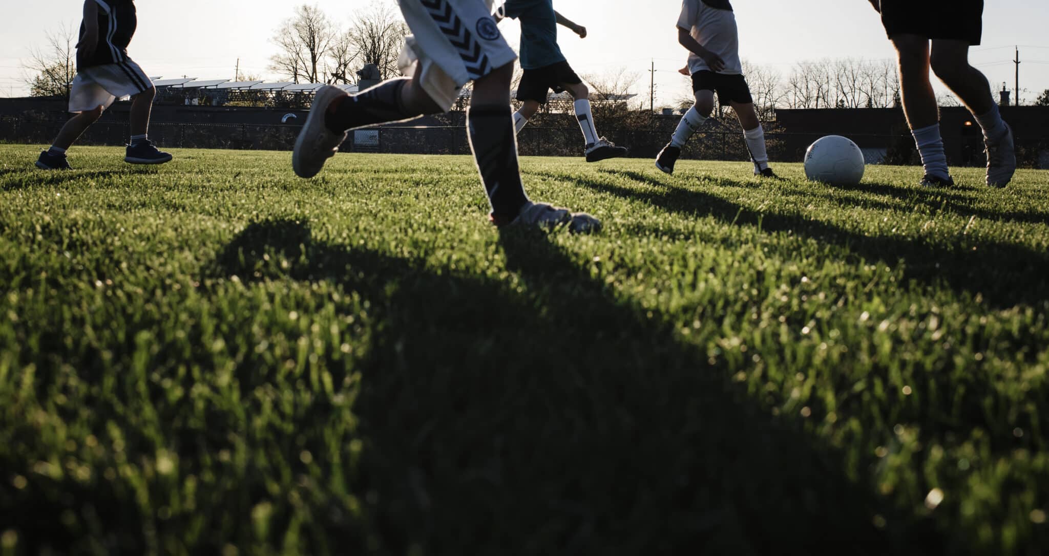 Low section of man playing soccer with children on grassy field at park during sunset