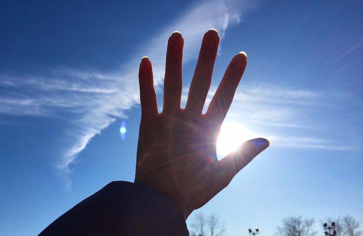 A hand held up against the sky partially shields the sun