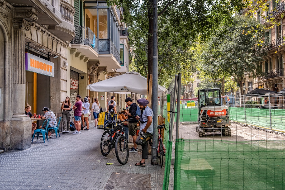 The Barcelona City Council has begun adding more green space to one of the main streets of the Eixample. Tourists and delivery men stand near the construction outside of the Hideout bar