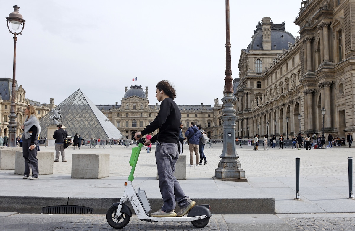 A man rides a Lime electric scooter in front of the Louvre in Paris