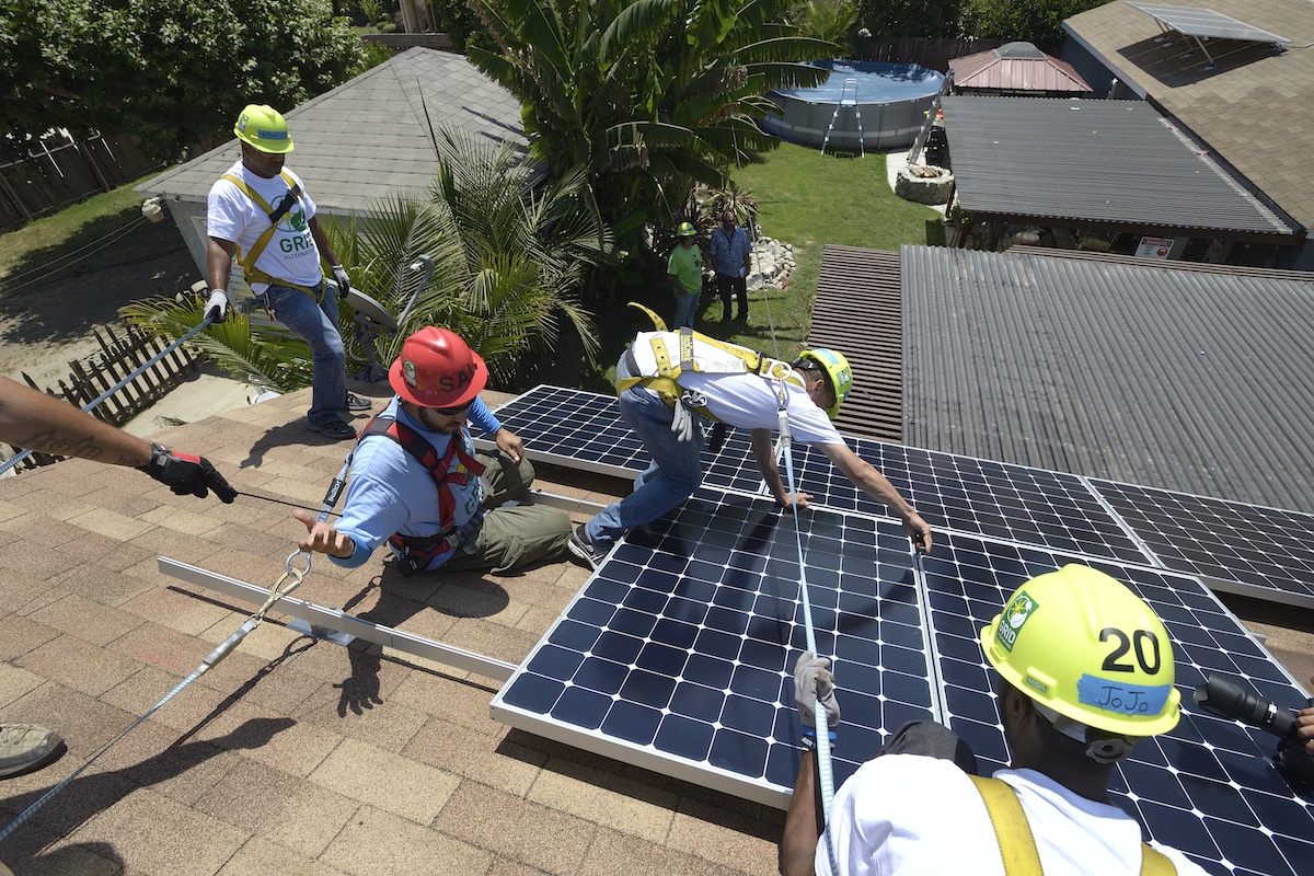 Workers install solar panels on the roof of a house in North Long Beach, California