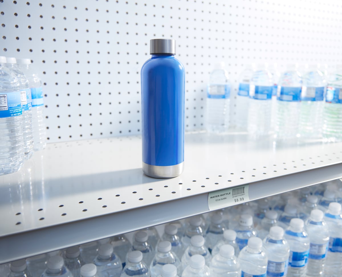 A reusable water bottle for sale on a store shelf surrounded by plastic single-use water bottles